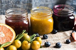 homemade jam in three jars with fruits surrounding it